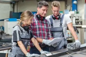 Azubis im Handwerkerbetrieb bekommen vom Gesellen etwas auf einem Zettel präsentiert