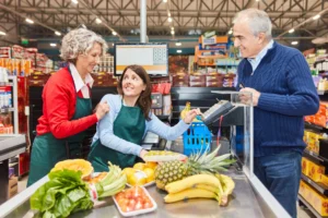 Verkäuferin hilft Azubi an der Supermarktkasse