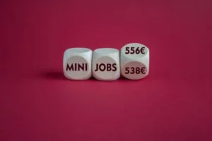 Würfel mit Symbol für die Anhebung der Einkommensgrenze für steuerfreie Minijobs in Deutschland von 538 Euro auf 556 Euro im Jahr 2025. Schöner roter Hintergrund. Geschäftskonzept.