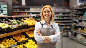 Supermarktverkäuferin steht in der Gemüseabteilung und lächelt freundlich.
