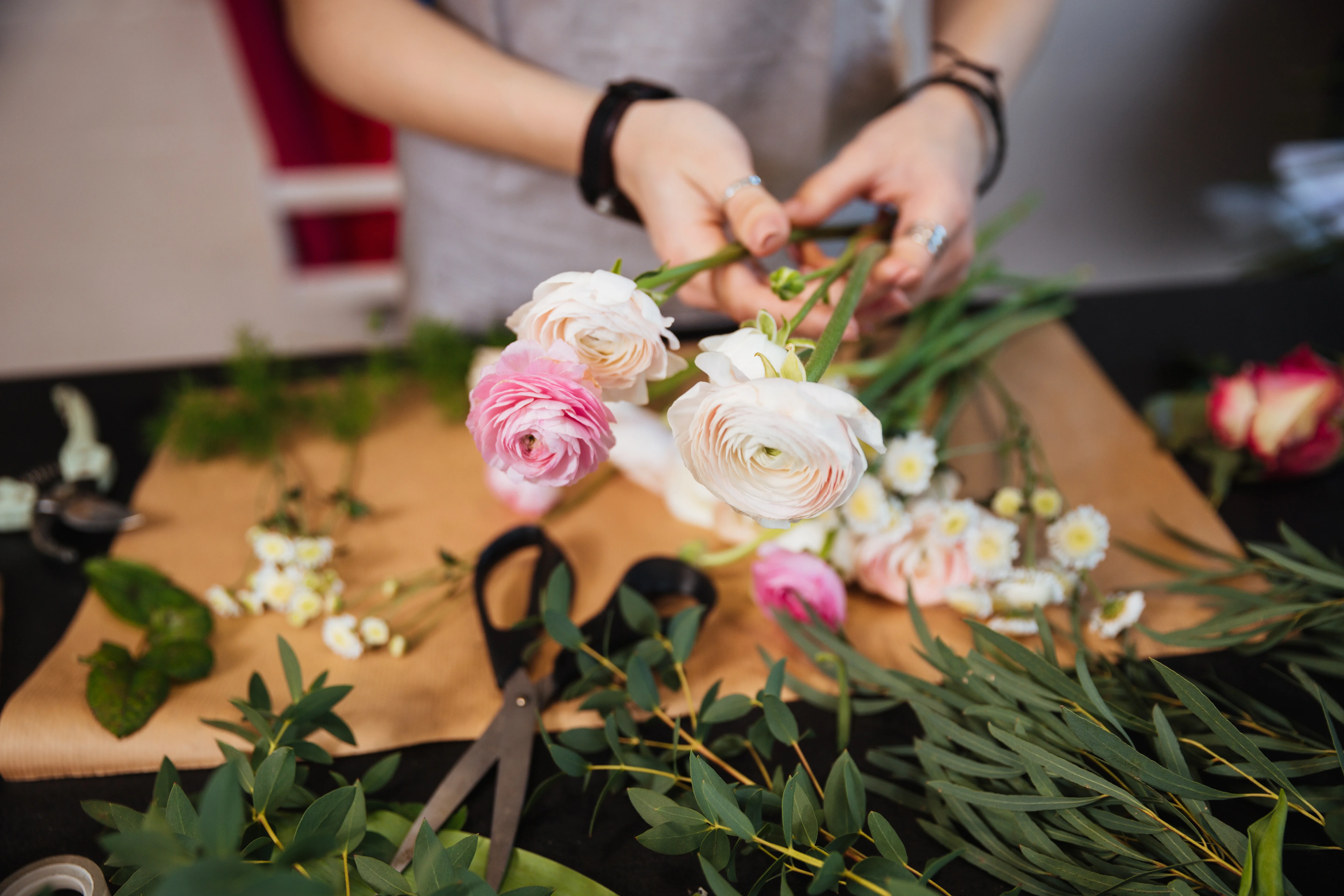 Hände arrangieren rosa und weiße Blumen mit Grünpflanzen auf einem Arbeitstisch